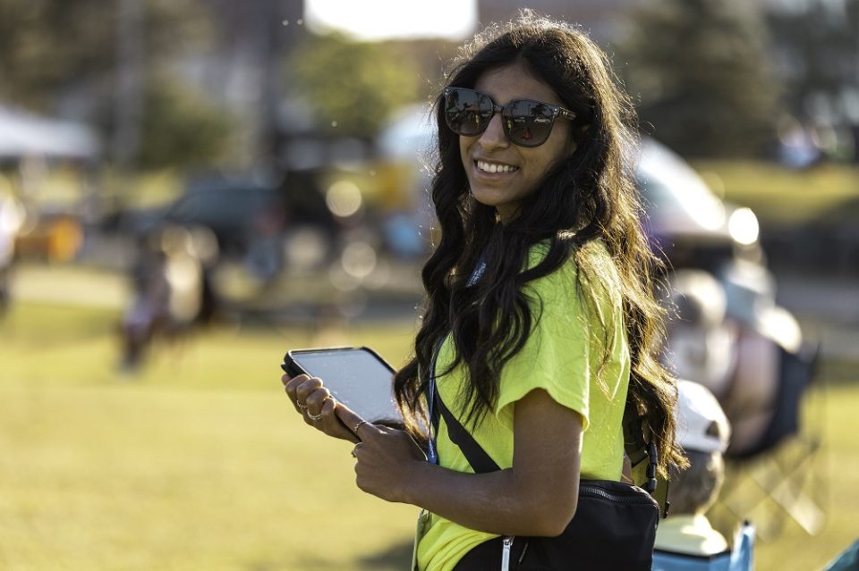 A volunteer in a bright yellow shirt holds an ipad for surveys at an outdoor concert