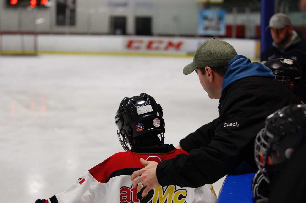 Image of a coach helping a young hockey player on the ice.