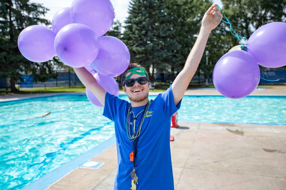 A lifeguard wearing a blue uniform is holding up balloons
