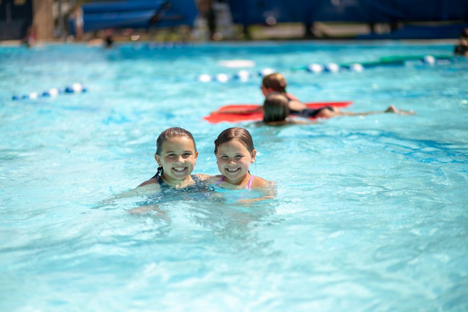 Two girls smiling in an outdoor swimming pool